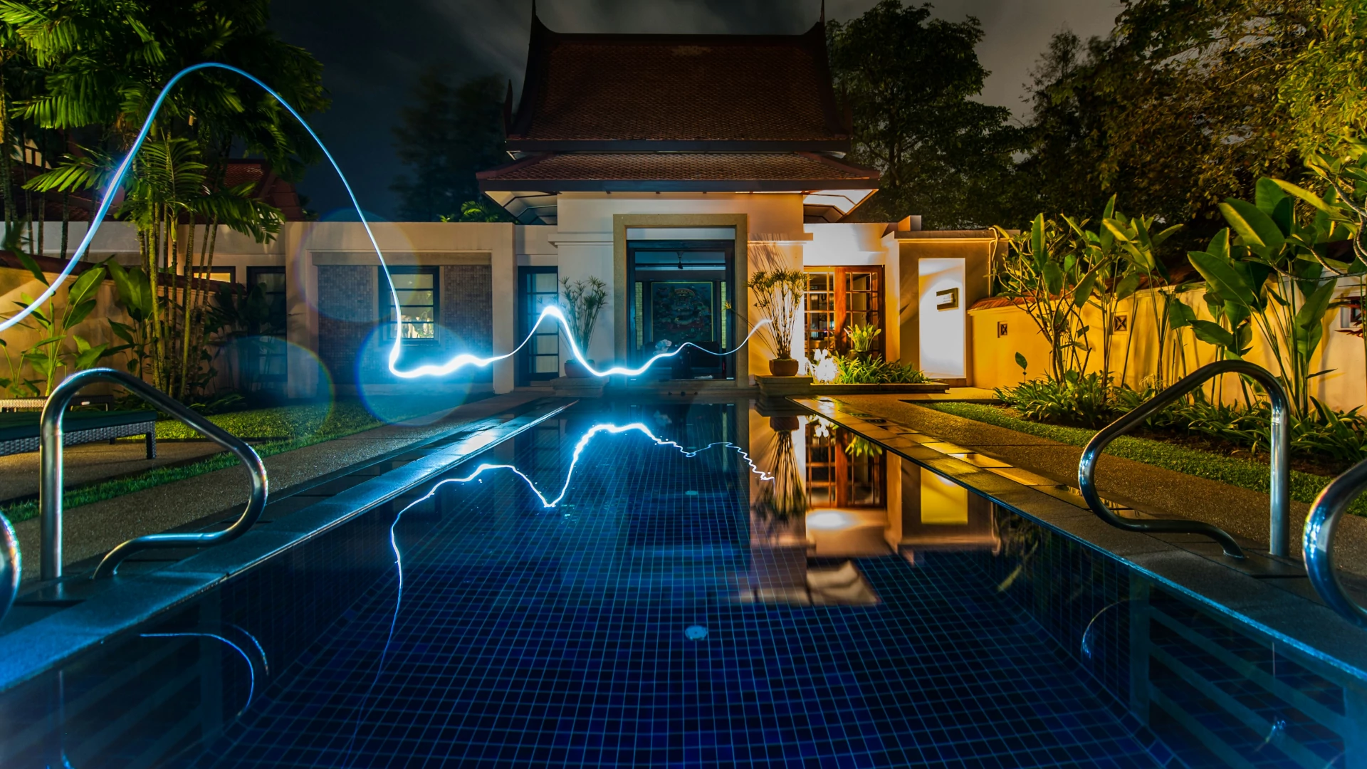 Efektowna fotografia nocna luksusowej posiadłości z basenem i dynamicznymi smugami światła, symbolizującymi zasilanie i przepływ energii w inteligentnym systemie smart home Home Center.